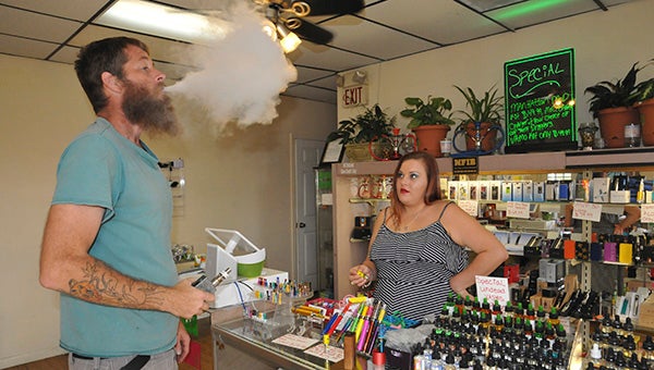 HEALTHIER ALTERNATIVE: From left, Big Time Vapes’ customer Scott DoLittle blows smoke, while Dudziak’s daughter Erika Forbes waits on him.  Photo by Cassandra Favre 